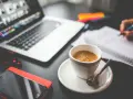 Tazza di caffè, laptop, smartphone e mani che scrivono su un quaderno. Questo è cosa significa da remoto: lavorare ovunque.