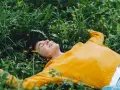 Persona sorridente sdraiata nell'erba verde con piccoli fiori gialli, godendosi un momento di digital detox.