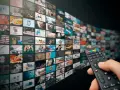 Un telecomando seleziona contenuti da un muro di schermi, offrendo un'ampia scelta di video on demand.