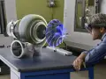 Un uomo con visore AR studia un ologramma di un turbocompressore, esplorando il suo significato tecnologico in officina.