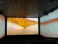 Schermo gigante in un cinema, con un paesaggio montano dorato proiettato. L'esperienza immersiva del cinema.
