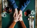 Mani che si stringono a tavola, bicchieri di vino rosso. Un momento intimo, ma il suo sguardo è perso, un red flag significato di pensieri lontani.