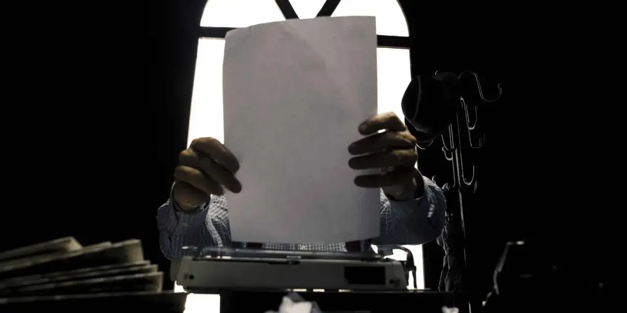 Un giornalista, con foglio bianco e macchina da scrivere, cerca il significato delle parole.