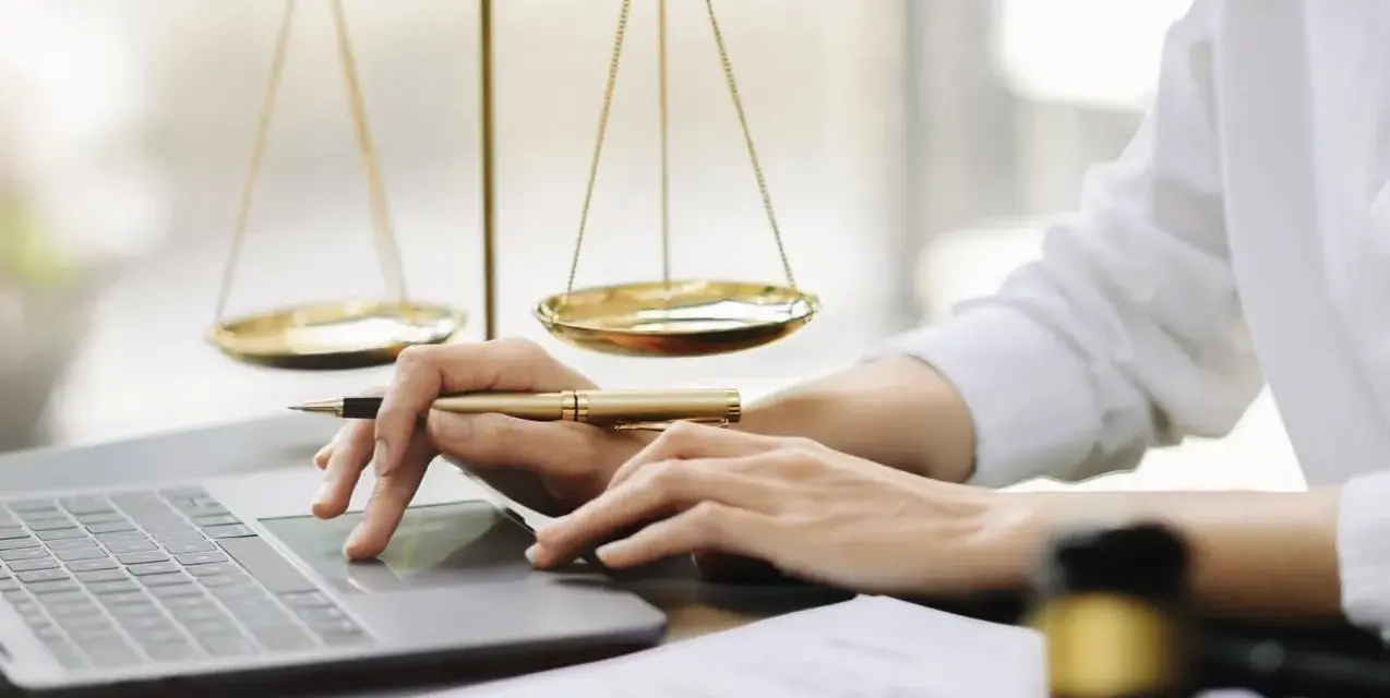 Mani che lavorano al computer, con bilancia della giustizia e martelletto. Uno smart worker legale.