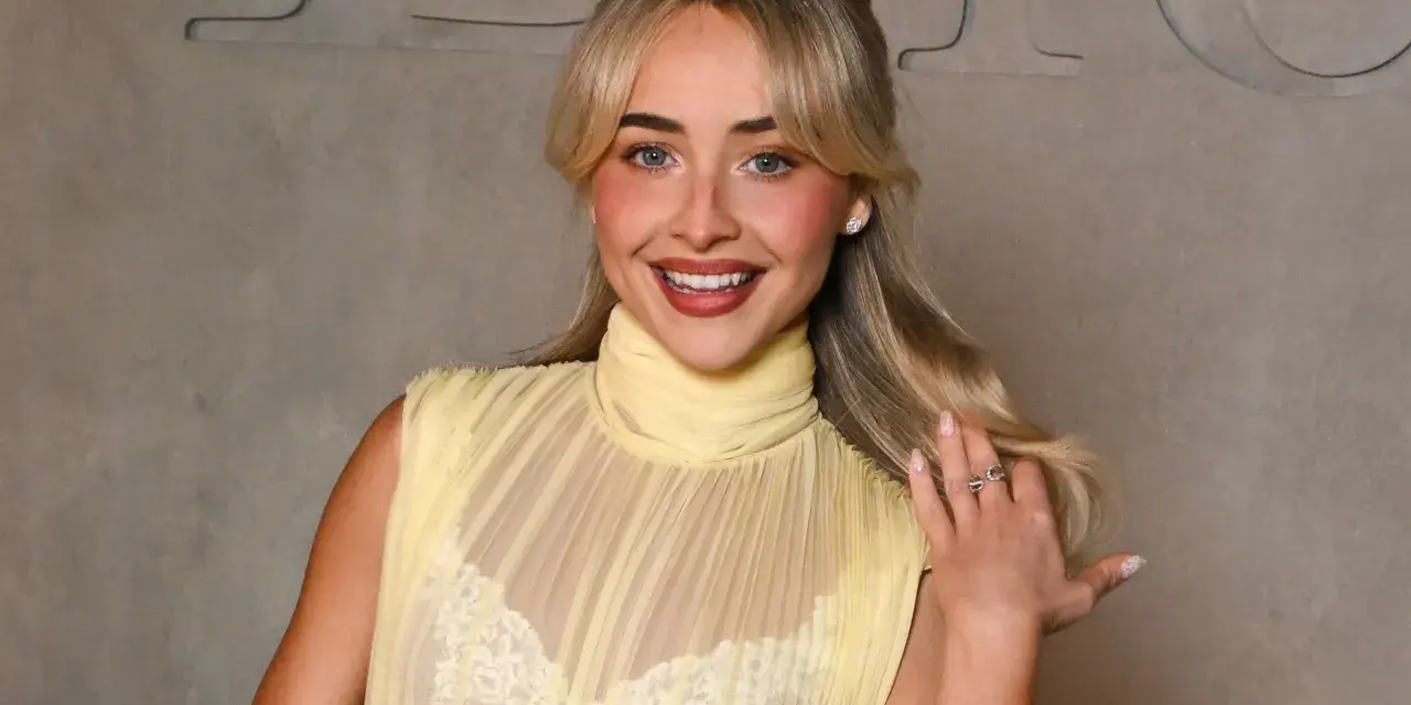 Una ragazza sorride, indossa un abito giallo trasparente con un reggiseno di pizzo bianco visibile.