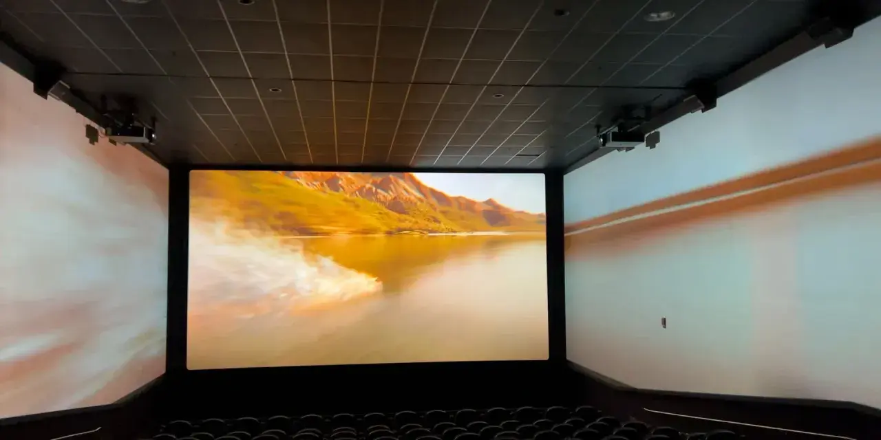 Schermo gigante in un cinema, con un paesaggio montano dorato proiettato. L'esperienza immersiva del cinema.