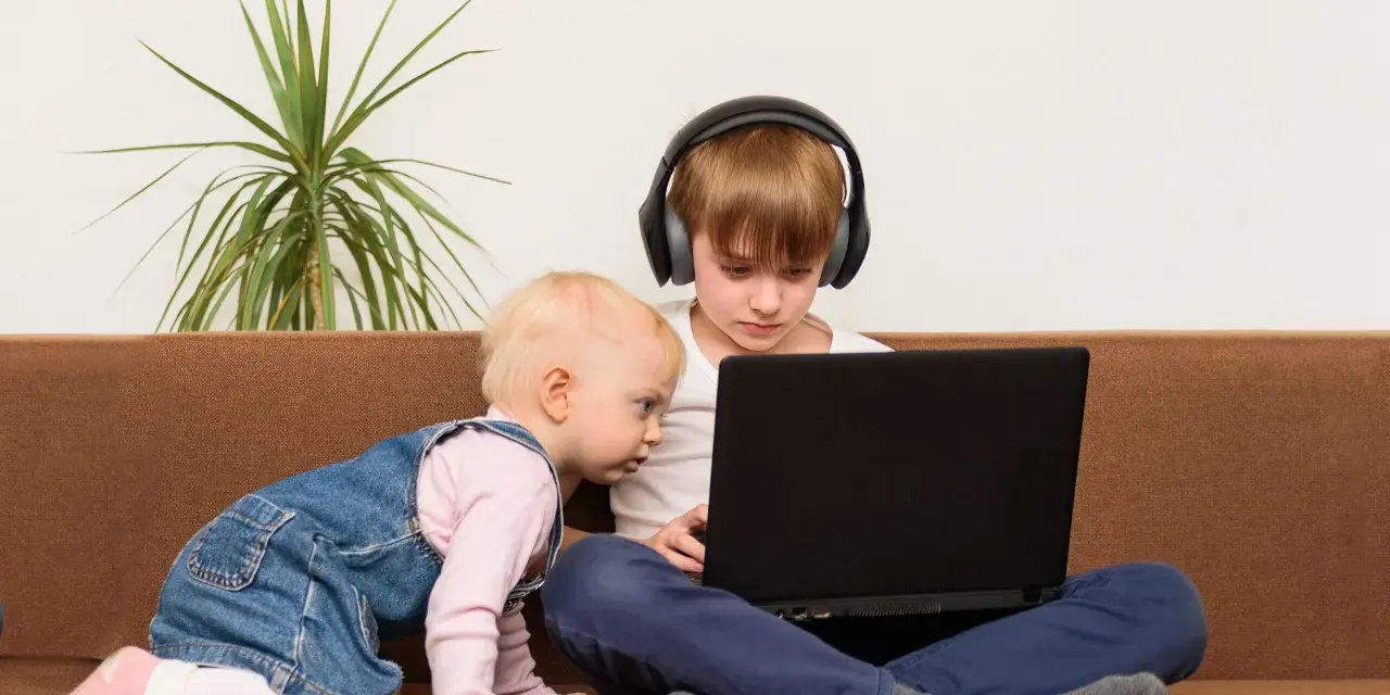 Bambini curiosi, forse la generazione dei 2012, esplorano un laptop. Uno con cuffie, l'altro gattona.