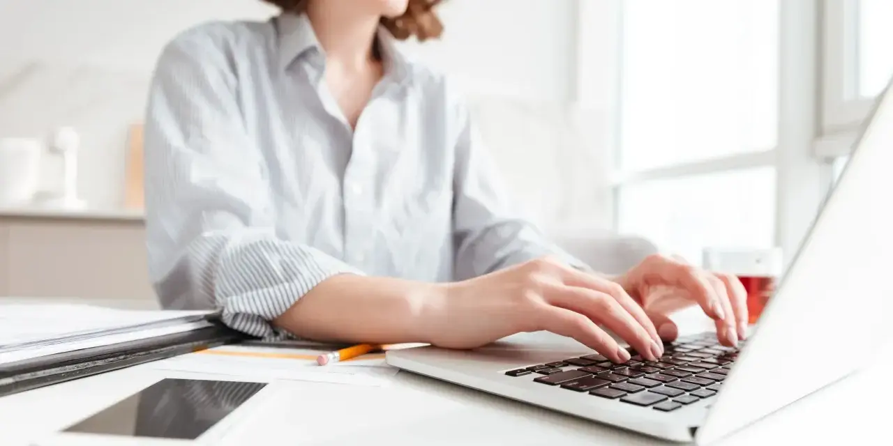 Donna sorridente al computer, che lavora per scoprire quanto si guadagna con Shopify. Sul tavolo, smartphone e documenti.