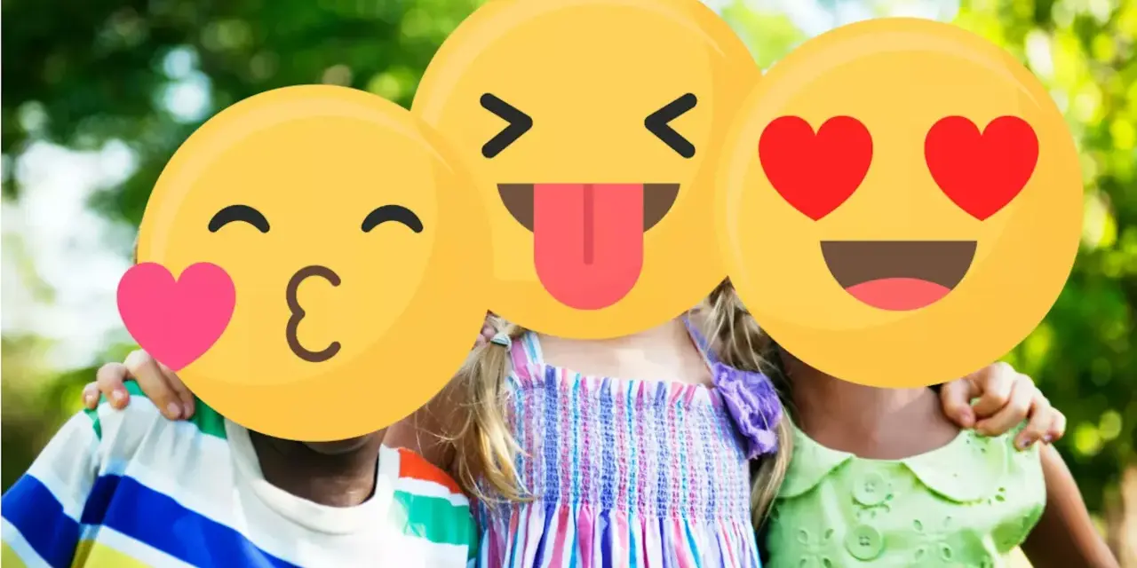 Tre bambini sorridono all'aperto, con emoji che coprono i loro volti. Un esempio di sharenting, condividere momenti felici online.