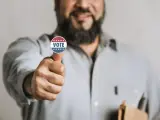 Uomo con adesivo "VOTE" sul pollice, un gesto di approvazione che simboleggia l'endorsement significato politico.