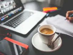 Tazza di caffè, laptop, smartphone e mani che scrivono su un quaderno. Questo è cosa significa da remoto: lavorare ovunque.