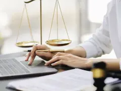Mani che lavorano al computer, con bilancia della giustizia e martelletto. Uno smart worker legale.