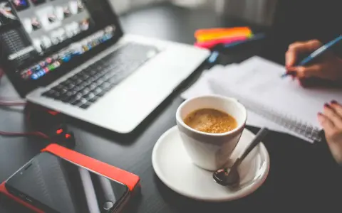Tazza di caffè, laptop, smartphone e mani che scrivono su un quaderno. Questo è cosa significa da remoto: lavorare ovunque.