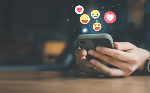 Mani che scorrono su uno smartphone, con emoji che fluttuano, simbolo di un efficace buzz marketing e interazione sui social media.