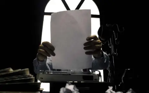 Un giornalista, con foglio bianco e macchina da scrivere, cerca il significato delle parole.