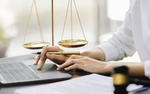 Mani che lavorano al computer, con bilancia della giustizia e martelletto. Uno smart worker legale.