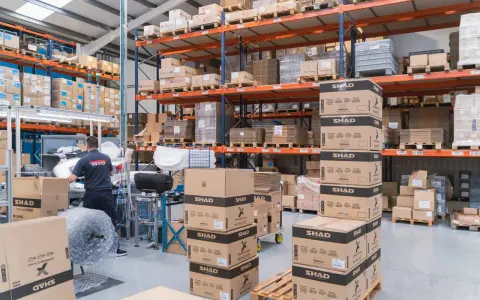 Magazzino pieno di scatoloni SHAD, pronti per spedizioni in un volatile ecommerce. Un lavoratore sistema la merce.