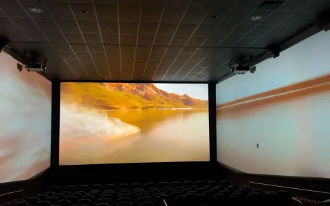 Schermo gigante in un cinema, con un paesaggio montano dorato proiettato. L'esperienza immersiva del cinema.
