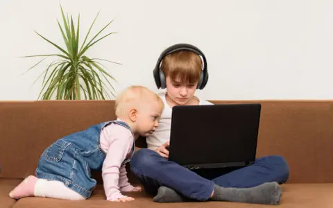 Bambini curiosi, forse la generazione dei 2012, esplorano un laptop. Uno con cuffie, l'altro gattona.