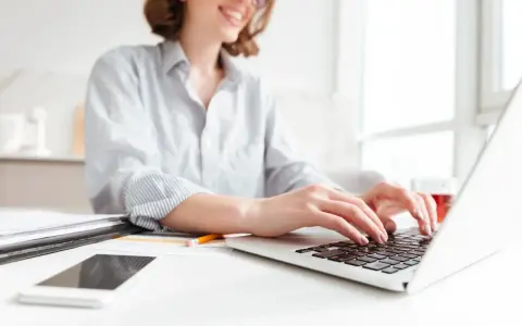 Donna sorridente al computer, che lavora per scoprire quanto si guadagna con Shopify. Sul tavolo, smartphone e documenti.