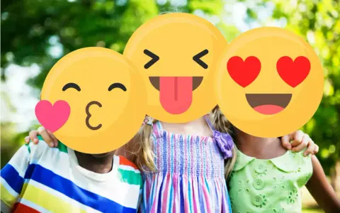 Tre bambini sorridono all'aperto, con emoji che coprono i loro volti. Un esempio di sharenting, condividere momenti felici online.