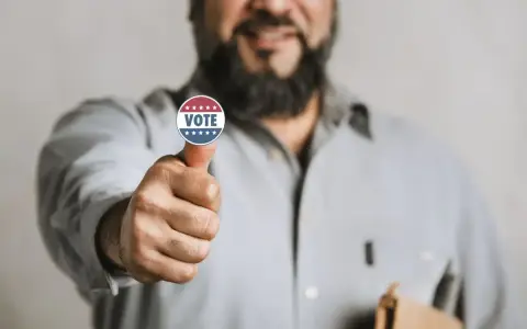 Uomo con adesivo "VOTE" sul pollice, un gesto di approvazione che simboleggia l'endorsement significato politico.