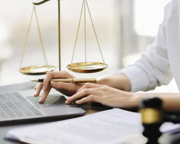 Mani che lavorano al computer, con bilancia della giustizia e martelletto. Uno smart worker legale.