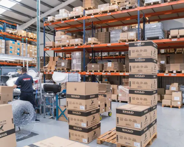 Magazzino pieno di scatoloni SHAD, pronti per spedizioni in un volatile ecommerce. Un lavoratore sistema la merce.