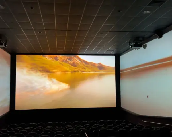 Schermo gigante in un cinema, con un paesaggio montano dorato proiettato. L'esperienza immersiva del cinema.