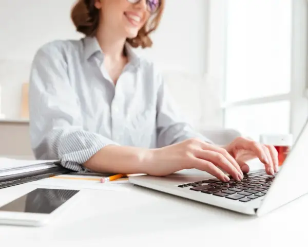Donna sorridente al computer, che lavora per scoprire quanto si guadagna con Shopify. Sul tavolo, smartphone e documenti.