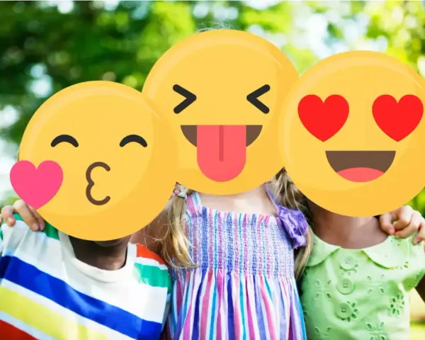 Tre bambini sorridono all'aperto, con emoji che coprono i loro volti. Un esempio di sharenting, condividere momenti felici online.
