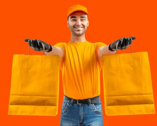 Un rider di Glovo azienda, con guanti neri e maglia gialla, porge due borse arancioni.
