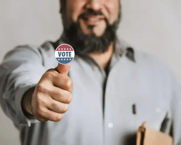 Uomo con adesivo "VOTE" sul pollice, un gesto di approvazione che simboleggia l'endorsement significato politico.
