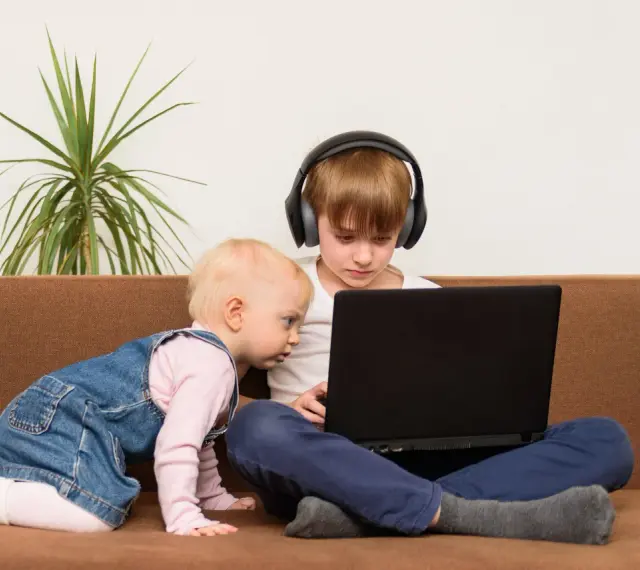Bambini curiosi, forse la generazione dei 2012, esplorano un laptop. Uno con cuffie, l'altro gattona.