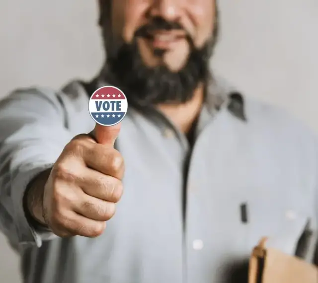 Uomo con adesivo "VOTE" sul pollice, un gesto di approvazione che simboleggia l'endorsement significato politico.