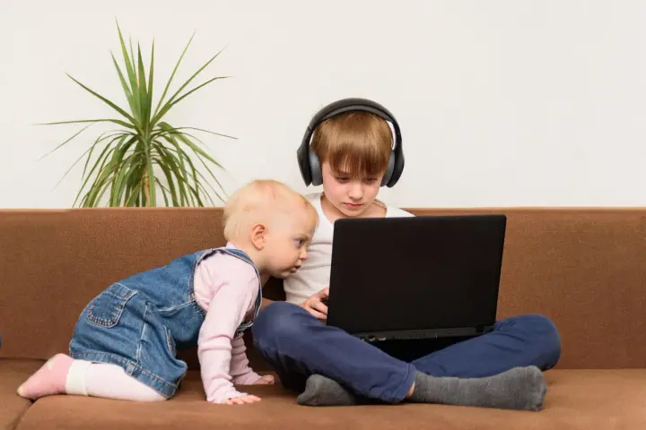 Bambini curiosi, forse la generazione dei 2012, esplorano un laptop. Uno con cuffie, l'altro gattona.
