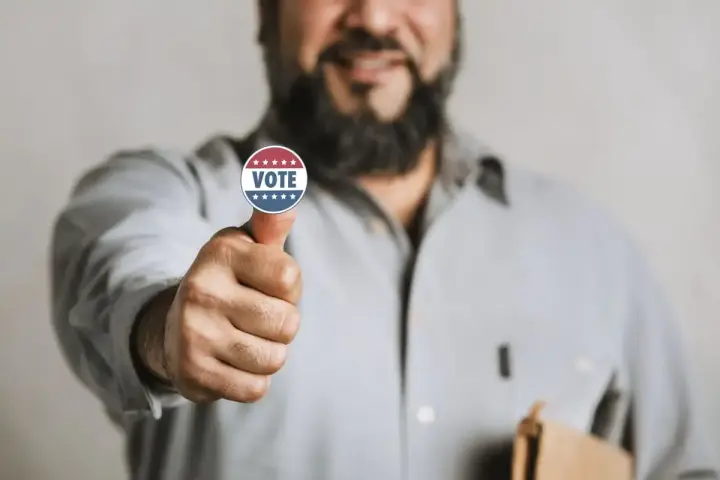 Uomo con adesivo "VOTE" sul pollice, un gesto di approvazione che simboleggia l'endorsement significato politico.