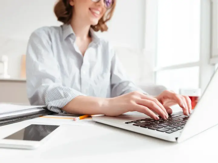 Donna sorridente al computer, che lavora per scoprire quanto si guadagna con Shopify. Sul tavolo, smartphone e documenti.