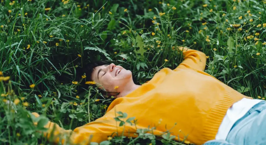 Persona sorridente sdraiata nell'erba verde con piccoli fiori gialli, godendosi un momento di digital detox.