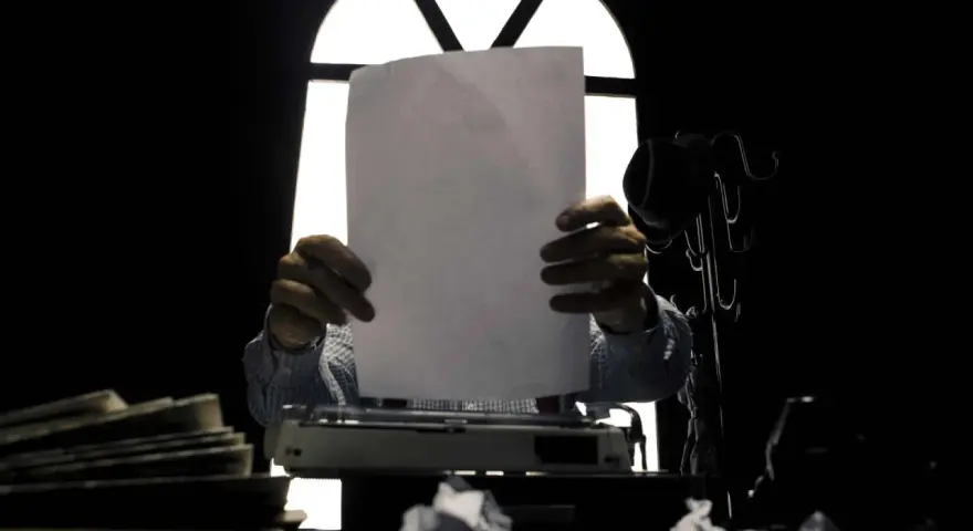 Un giornalista, con foglio bianco e macchina da scrivere, cerca il significato delle parole.