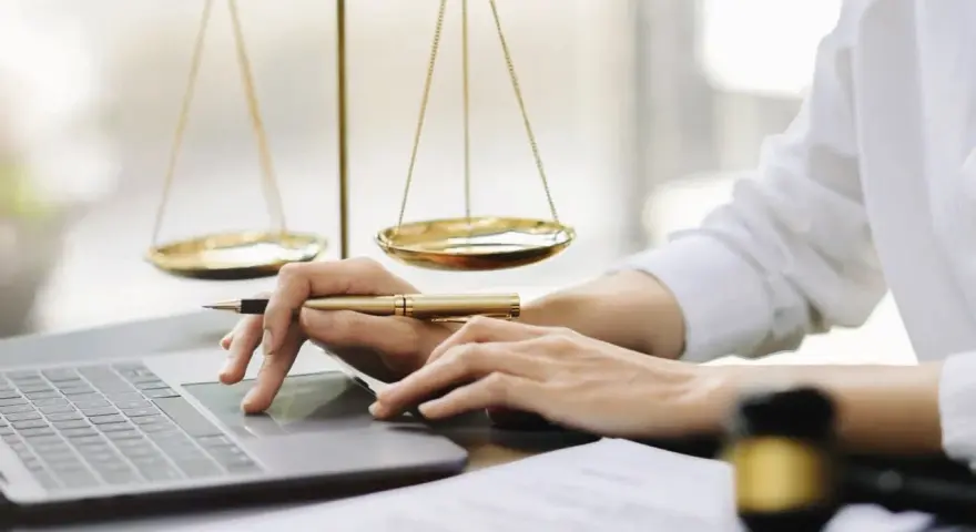 Mani che lavorano al computer, con bilancia della giustizia e martelletto. Uno smart worker legale.