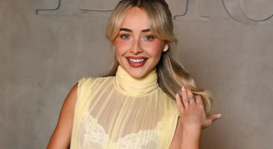 Una ragazza sorride, indossa un abito giallo trasparente con un reggiseno di pizzo bianco visibile.