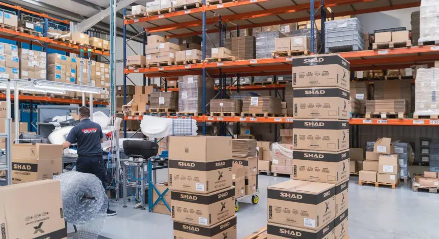 Magazzino pieno di scatoloni SHAD, pronti per spedizioni in un volatile ecommerce. Un lavoratore sistema la merce.