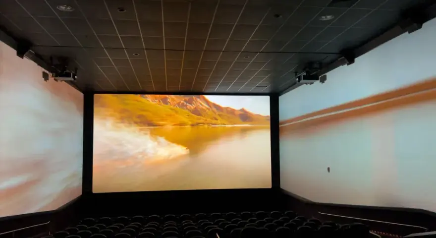 Schermo gigante in un cinema, con un paesaggio montano dorato proiettato. L'esperienza immersiva del cinema.