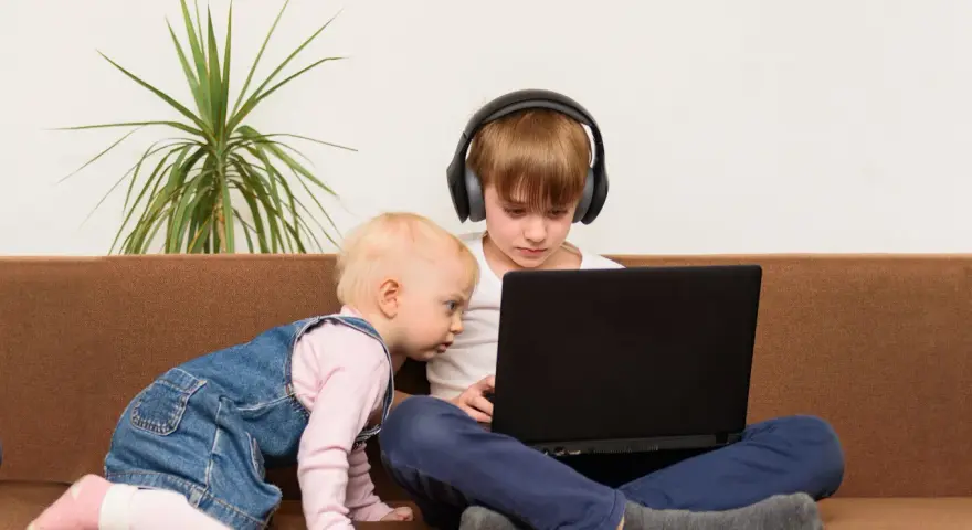 Bambini curiosi, forse la generazione dei 2012, esplorano un laptop. Uno con cuffie, l'altro gattona.
