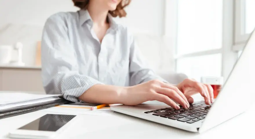 Donna sorridente al computer, che lavora per scoprire quanto si guadagna con Shopify. Sul tavolo, smartphone e documenti.