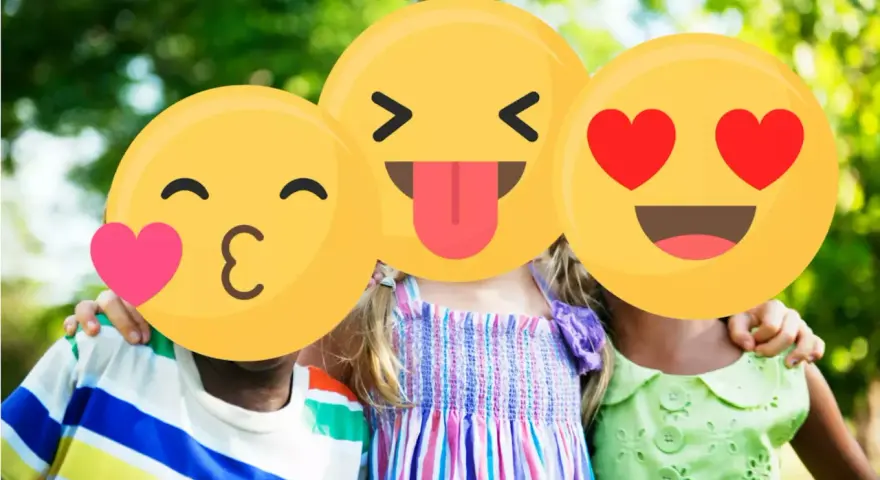 Tre bambini sorridono all'aperto, con emoji che coprono i loro volti. Un esempio di sharenting, condividere momenti felici online.