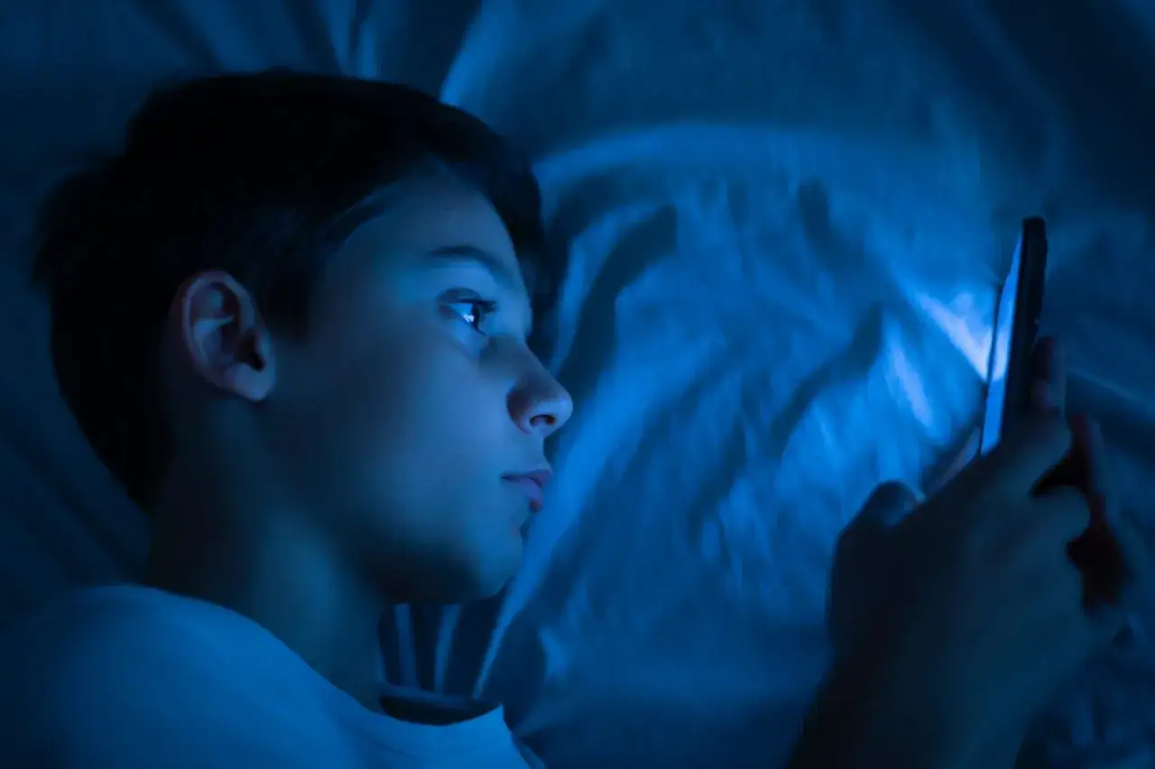 Ragazzo a letto, illuminato dal telefono, che forse scopre il cringe significato in italiano.