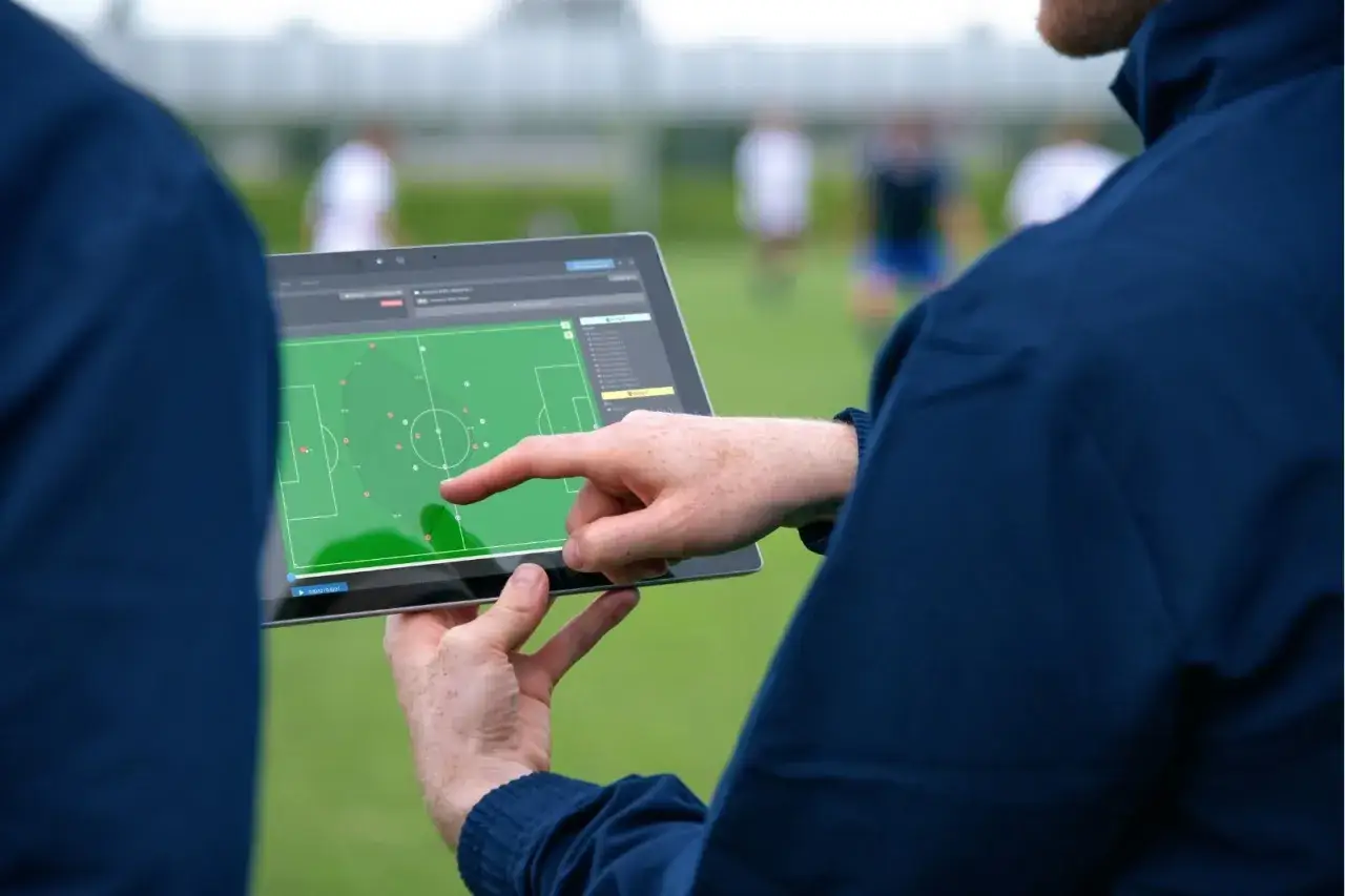 Allenatore analizza tattiche di calcio su tablet, mostrando la tecnologia nello sport.